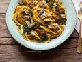 Un piatto di pasta con le sarde, condita con erbe aromatiche, pinoli e pangrattato tostato, servita su un piatto azzurro.
