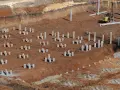Plac budowy z licznymi betonowymi słupami, tworzącymi fundament pośredni. W tle maszyna budowlana.