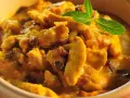 Pyszny kurczak w sosie curry z rodzynkami, ozdobiony listkiem mięty. Idealny przykład, jak zrobić sos curry do kurczaka.