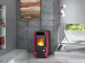 Estufa roja moderna con fuego encendido, mostrando cómo funciona la biomasa. Estantería blanca con libros y sillones blancos al fondo.