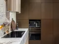 Nowoczesne wykończenie szafek kuchennych górnych w kolorze brązu, z wbudowanym ekspresem do kawy i płytą indukcyjną na tle marmurowego blatu.