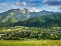 Malowniczy widok na Tatry z Jaszczurówki, gdzie liczne atrakcje czekają na turystów. Zielone wzgórza i tradycyjna zabudowa tworzą sielski krajobraz.