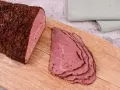 Pastrami co to? Aromatyczny, peklowany i wędzony kawałek wołowiny, pokrojony w cienkie plastry, leżący na desce.