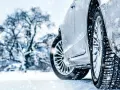Auto im Schnee mit Winterreifen, verschneiter Baum im Hintergrund.