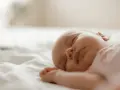 Śpiące niemowlę na białej pościeli.