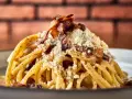 Pyszny makaron włoski carbonara z chrupiącym boczkiem i parmezanem, posypany świeżo mielonym pieprzem.