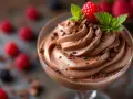 Délicieux dessert sans oeuf : mousse au chocolat onctueuse, garnie de copeaux de chocolat, d'une framboise fraîche et de feuilles de menthe.
