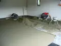 Dwóch budowlańców pracuje przy wylewce podłogi. W tle widać maszynę, która wygląda jak **mixokret**.