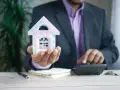 Hombre con traje calcula cuánto puede subir el alquiler, sosteniendo una casa de juguete.