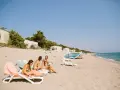 Trzy osoby relaksują się na plaży w nudystycznym obozie, siedząc na leżakach. Jeden z nich trzyma piłkę.