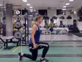 Kvinna utför utfallssteg med vikt i ett gym. Hon håller en hantel i ena handen och har ett ben framåt och ett bakåt.