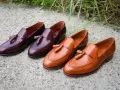 Eleganckie, skórzane loufersy z chwostami w kolorze koniaku i burgundu, ułożone na betonowej nawierzchni.