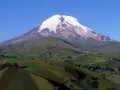 Pokryty śniegiem wulkan Chimborazo, jeden z najwyższych gór świata, góruje nad zielonymi, pofałdowanymi wzgórzami z polami uprawnymi.