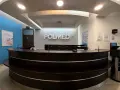 Recepcja kliniki medycznej POLMED z ciemnobrązowym ladą i logo na ścianie.