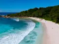 Rajska wyspa na Oceanie Indyjskim. Turkusowa woda obmywa piaszczystą plażę, a bujna zieleń porasta wzgórza.