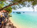Drewniana kładka prowadzi do krystalicznie czystej wody na plaży. Łodzie kołyszą się na turkusowym morzu. Rajskie wakacje na Zanzibarze.
