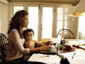 Una mamma lavoratrice con il suo bambino in grembo, mentre digita al computer tra libri e fogli.