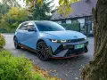 Niebieski Hyundai Ioniq 5 N z czerwonymi akcentami stoi na tle domu i drzew.