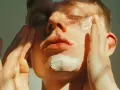 Un joven se aplica crema en el rostro, cubriendo un pequeño punto negro enquistado.