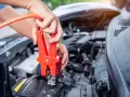 Hands connect jumper cables to a car battery, a common fix when wondering how long can a car be on before the battery dies.