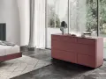 Cassettiera camera da letto moderna color bordeaux, con sei cassetti, accanto a un letto e una grande finestra.