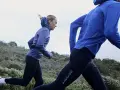 Två personer springer i en kuperad terräng. De är klädda i träningskläder och verkar inte bry sig om att det är lite grått ute, de njuter av att springa i regn.