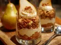 Postre de pera en vaso con crema y granola, acompañado de una pera entera.