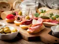 Pyszne tapas na drewnianej desce: pieczywo z wędliną, oliwkami, ogórkiem i suszonymi pomidorami.