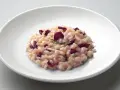 Un cremoso risotto al radicchio rosso, guarnito con erba cipollina, servito su un piatto bianco.