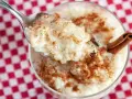 Cuchara con cremoso arroz con leche, espolvoreado con canela. ¿Quién inventó el arroz con leche? ¡Este postre es un clásico!