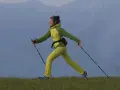 Donna sorridente pratica nordic walking su un prato. Informarsi sulle controindicazioni prima di iniziare.