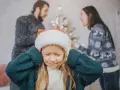 Ein Kind mit Weihnachtsmütze hält sich die Ohren zu, während die Eltern im Hintergrund streiten. Weihnachten trennen sie.