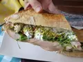 Bocadillo de pan rústico relleno de mortadela, burrata cremosa, rúcula, pistachos y tomates secos.