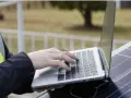 Praca nad projektem fotowoltaiki: ręce na klawiaturze laptopa, obok panel słoneczny.