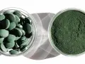 Dwie szklane miseczki: jedna z tabletkami chlorelli, druga z zielonym proszkiem. Dowiedz się, chlorella jak stosować, by czerpać z niej korzyści.