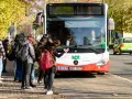 Ein Schulbus mit Warnblinker hält an einer Haltestelle. Schüler warten auf dem Gehweg, um einzusteigen.