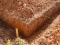 Wykonano wykop pod ławy fundamentowe. Widać ziemię, sznurki wyznaczające linie i drewniany palik.
