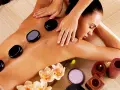 A woman enjoys the benefits of hot stone massage, with smooth black stones placed on her back. Orchids and candles add to the serene spa atmosphere.