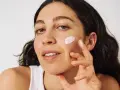 Frau mit zu Akne neigender Haut trägt eine leichte Creme auf.