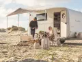 Ett par njuter av en stranddag med sina tyska husvagnar. Solen skiner och sanddynerna skapar en vacker bakgrund.
