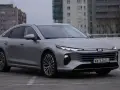 Srebrny Bestune B70 z nowoczesnymi światłami LED zaparkowany na betonowym placu, w tle budynki mieszkalne.