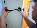 Un homme utilise un tournevis pour fixer une poignée de porte noire. Il est sur le point de lever la poignée pour fermer la porte.