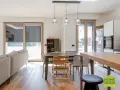 Un soggiorno luminoso con un divano, tavolo da pranzo e cucina a vista. Un moderno sopraluce illumina l'ambiente.