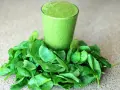 Un verre de smoothie vert entouré d'épinards frais, parfait pour un régime sans lectine.