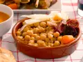 Cocido madrileño con garbanzos, chorizo, morcilla, patata y zanahoria en cuenco de barro.