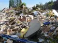 Ogromna kupa gruzów po zawaleniu się budynku. Widać izolację, drewno, beton i niebieską torbę. Wstęga policyjna zabezpiecza teren.