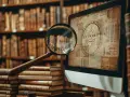 Loupe sur un écran affichant des documents anciens, évoquant la recherche de généalogie italienne gratuite en ligne parmi des livres d'histoire.