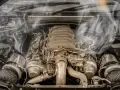 Smoke billows from a car's engine bay, indicating an engine overheating issue. The complex machinery sits idle, a testament to potential mechanical trouble.