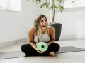 Lachende Frau mit Faszienrolle auf Yogamatte. Sie strahlt Lebensfreude aus und zeigt, wie man das positive sehen kann, auch nach dem Training.