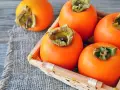Frische, orangefarbene Kaki-Früchte liegen in einem kleinen Korb auf grobem Leinen. Kaki gesund und lecker.